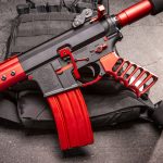 Custom AR-15 rifle in red and black, displayed on tactical vest.