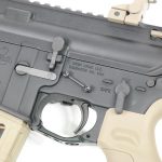 Close-up of black AR-style rifle receiver, showcasing precision engineering and ergonomic tan grip.