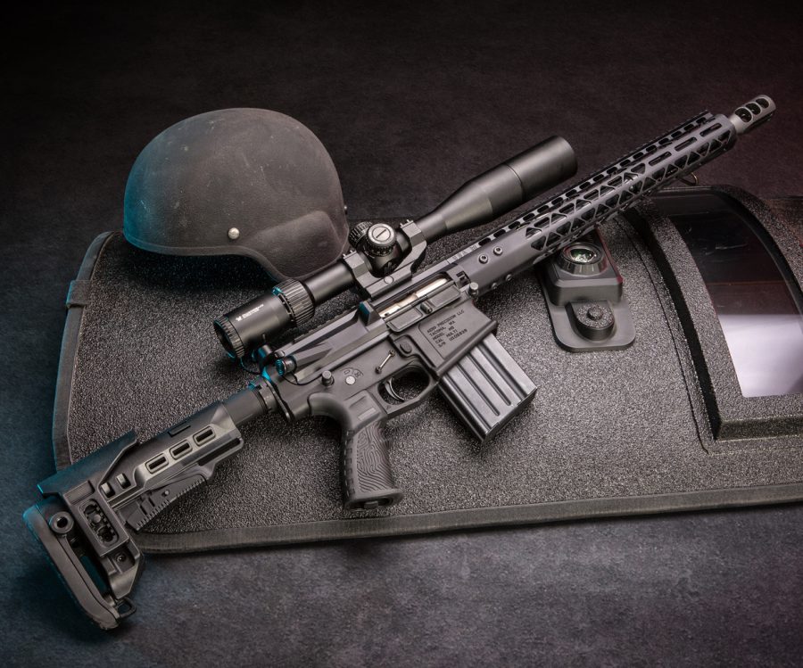 Modern tactical rifle with scope and helmet on textured surface for special ops use.