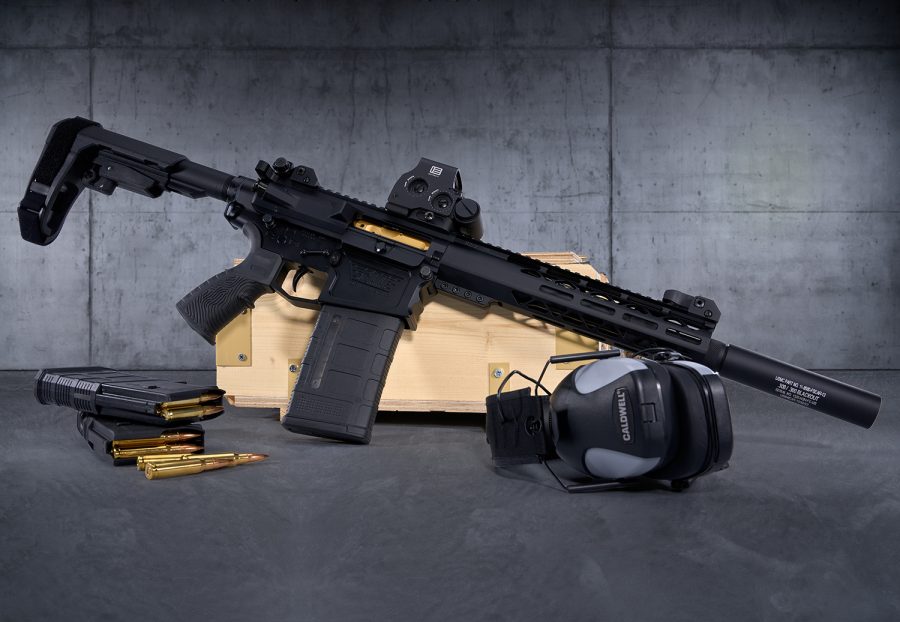 Modern tactical AR-style rifle with accessories on wooden crate against gray concrete background.