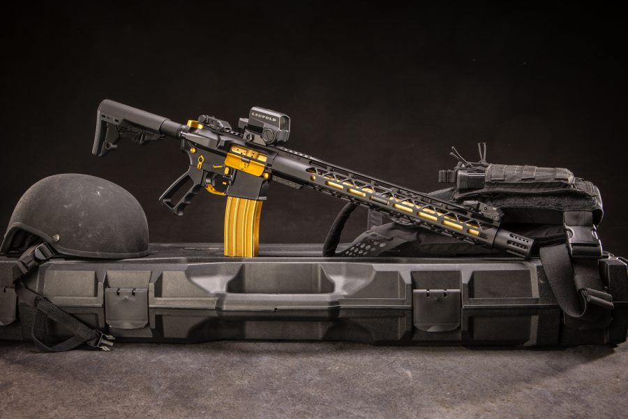 Black and gold custom AR rifle with Leupold optic, tactical gear, and ballistic helmet.