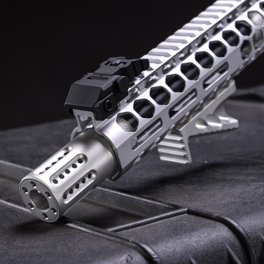 Close-up of modern firearm assembly with silver muzzle, honeycomb handguard, and Picatinny rail.