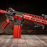 Red and Black Custom Tactical AR Rifle with Unique Aesthetic Displayed on Rustic Wooden Surface.
