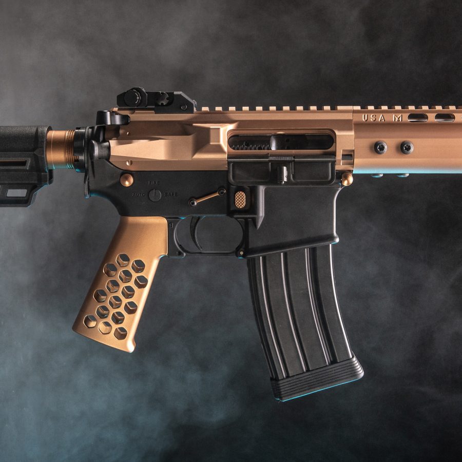 Copper-tone AR-style rifle with honeycomb grip against a dramatic smoky background.