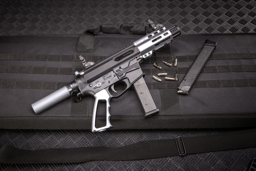 Silver tactical submachine gun with suppressor on padded case, ammo, and magazine visible nearby.