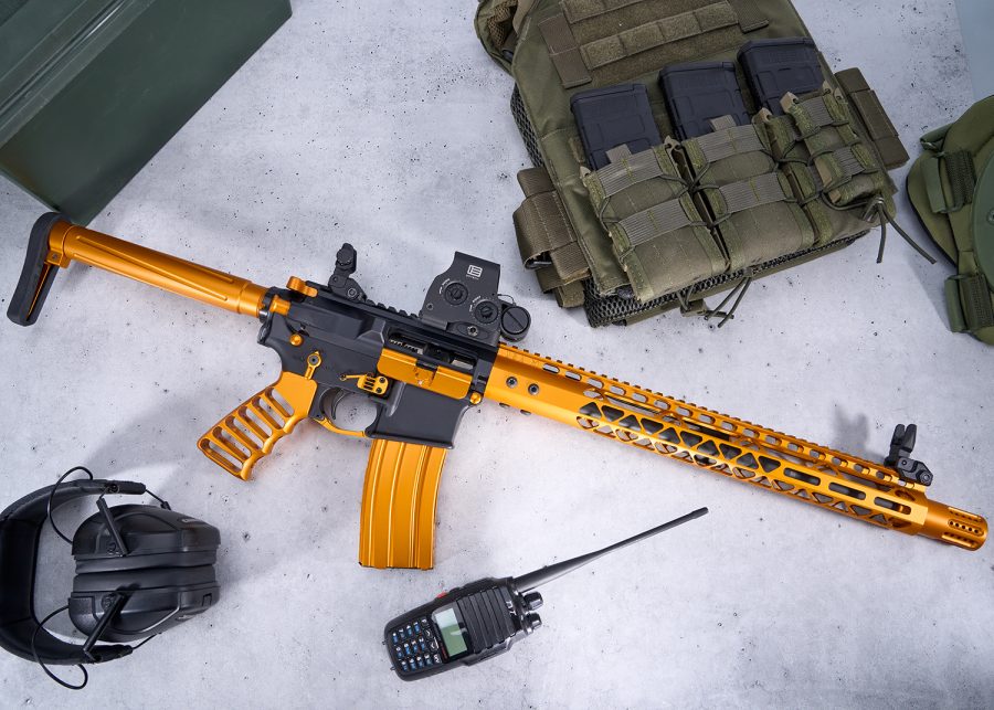 Custom gold and black AR rifle with tactical gear setup on concrete surface.