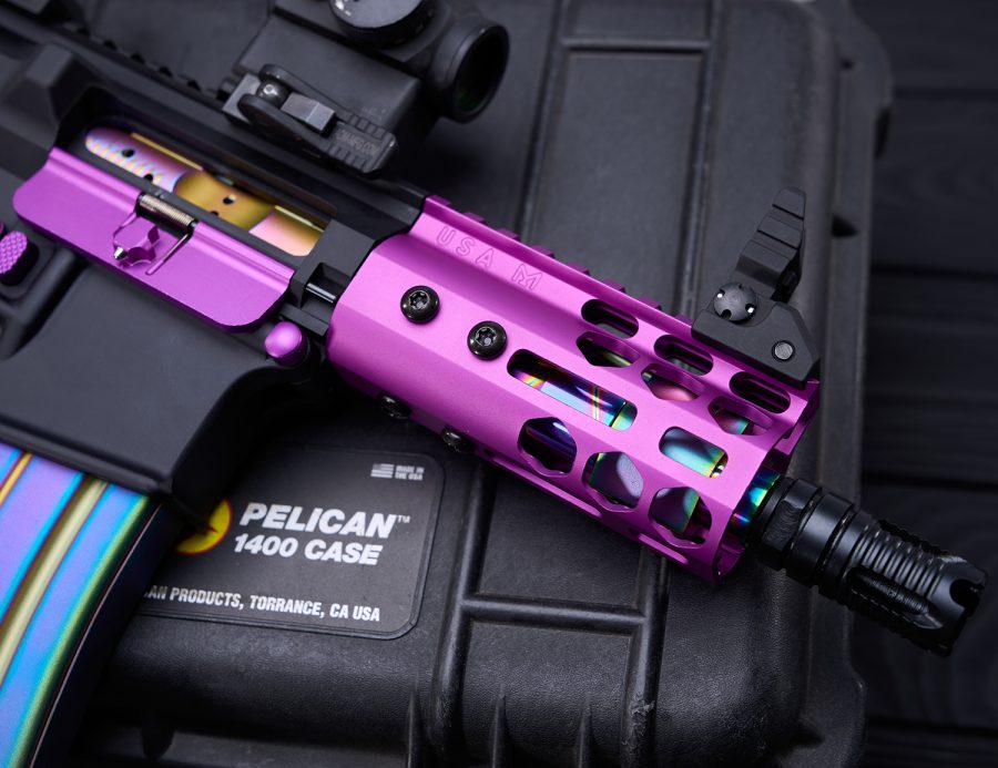 Custom tactical rifle with purple handguard on Pelican case, featuring red dot scope.