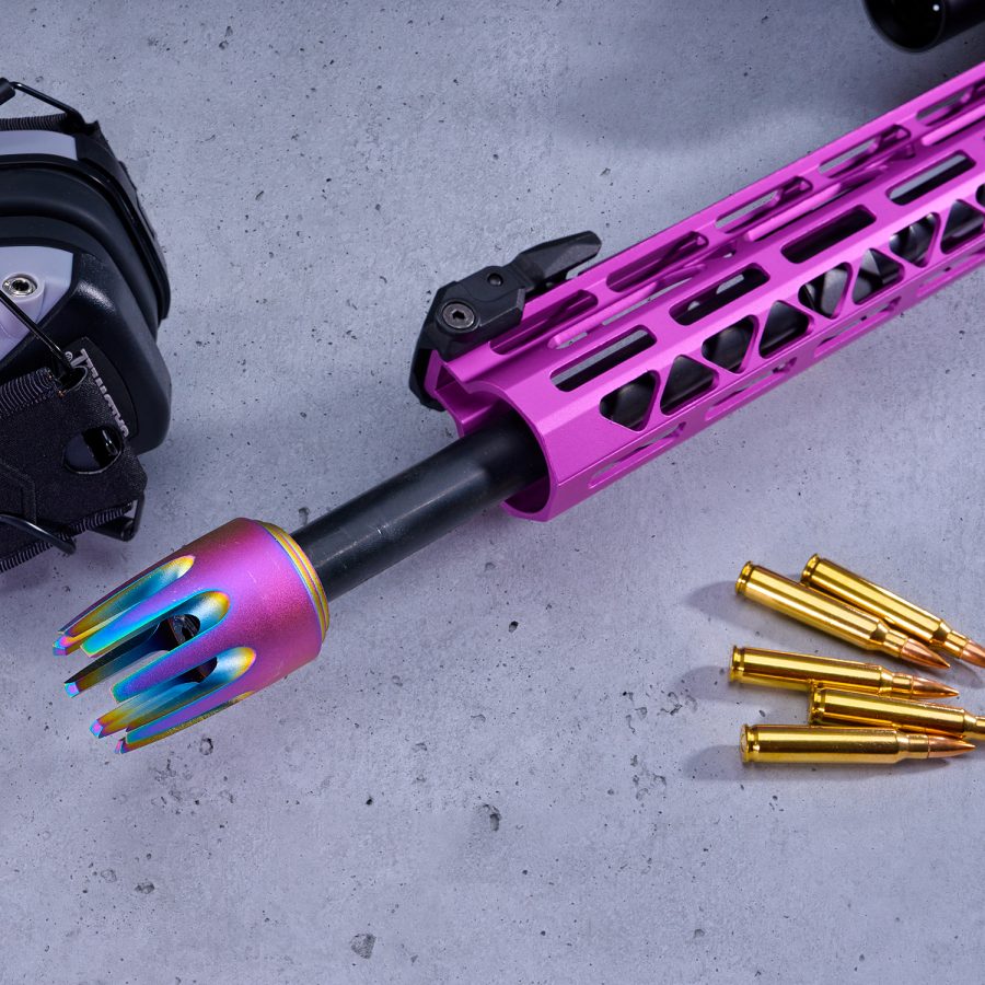 Pink firearm handguard with rainbow muzzle, brass cartridges, and black earmuffs on gray surface.