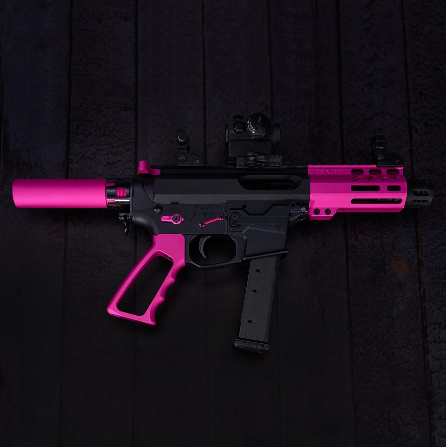 Custom pink and black AR-style pistol with optical sight on dark wooden background.