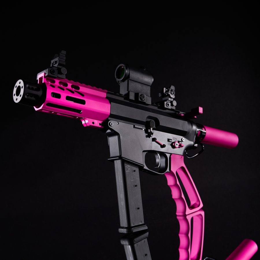 Vibrant pink and black AR-style rifle with tactical accessories against a black background.