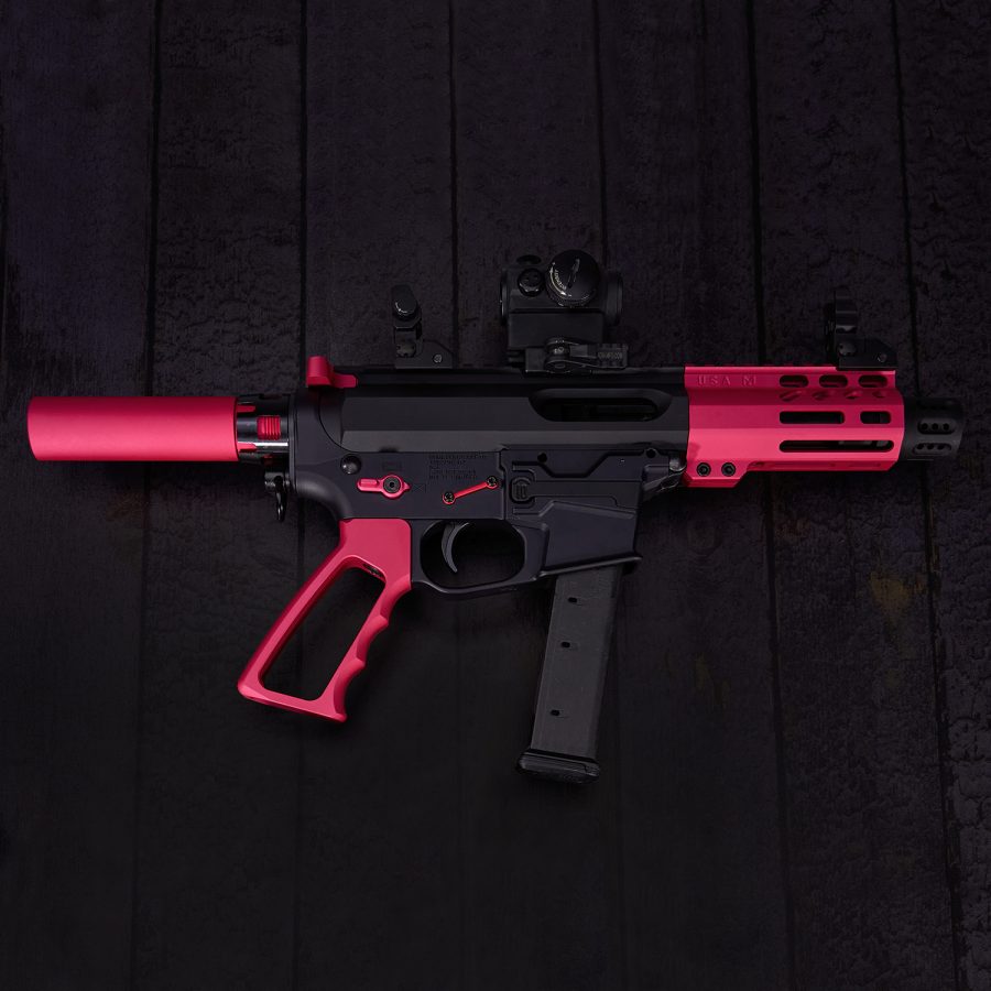 Hot pink and black AR-style pistol with custom components on wooden background.