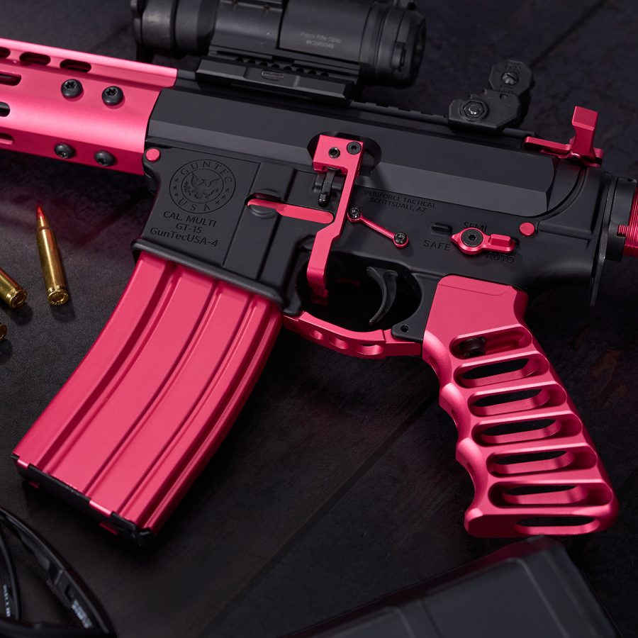 Custom black and hot pink AR-15 rifle with scope and brass rounds on dark surface.