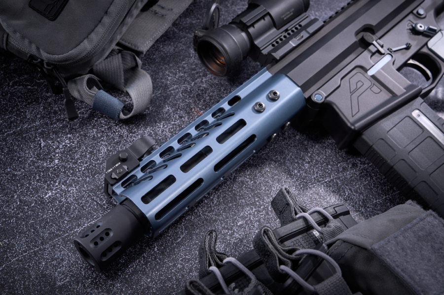 Modern tactical rifle with blue handguard, optic sight, on dark surface surrounded by gear.