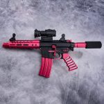 Pink and black AR-style rifle with tactical accessories on a gray concrete background.