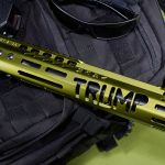 Olive-green tactical rail with TRUMP branding on black bag, sunglasses nearby.