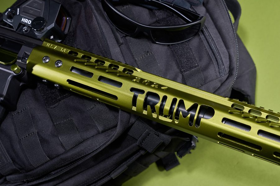 Olive-green tactical rail with TRUMP branding on black bag, sunglasses nearby.