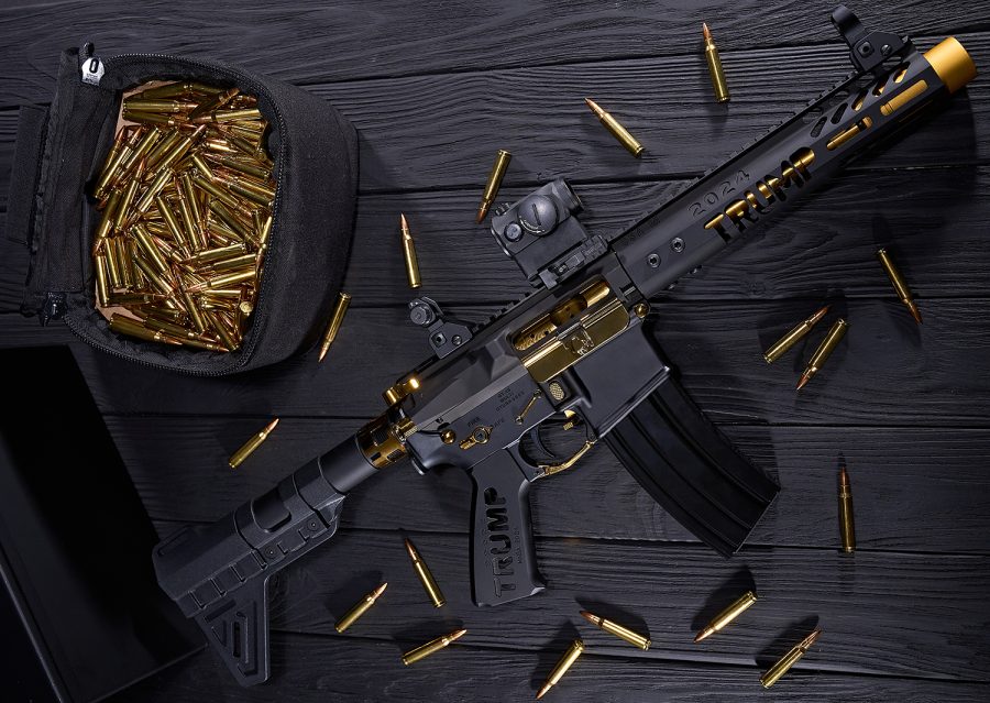 Custom black AR-style rifle with gold accents, TRUMP branding, tactical sight, and brass ammo.