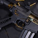Custom black and gold AR-15 rifle with Trump MAGA 2024 engravings, brass ammo shown.