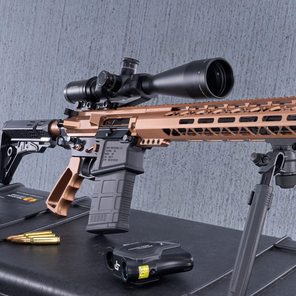 Custom AR-15 rifle with copper finish, long-range scope, displayed on black surface with cartridge nearby.